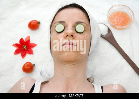 Weibliche Modell mit einer Tomate scrub aus frischen Tomaten, Kokosöl und Zucker mit Scheiben Gurke auf die Augen. Stockfoto