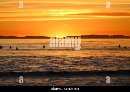 Orange Sonnenuntergang in Huntington Beach Kalifornien mit Surfern im Wasser warten auf Wellen Stockfoto