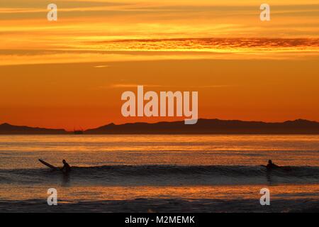 Orange Sonnenuntergang in Huntington Beach Kalifornien mit Surfern im Wasser warten auf Wellen Stockfoto