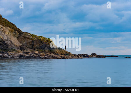 Ein junger Mann Fische aus den Felsen auf einen ruhigen Abend auf Cornwalls Polkerris Strand. Stockfoto