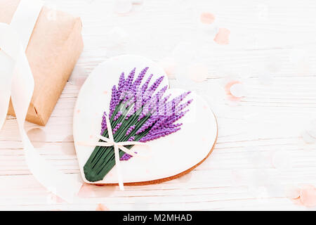 Happy Mother's Day Grußkarte. cookie Herz mit Lavendel Bouquet und Handwerk Geschenkbox auf weißen Holzmöbeln im Landhausstil Hintergrund mit Konfetti. Platz für Tex Stockfoto