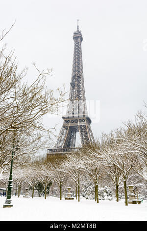 Winter in Paris im Schnee. Der Eiffelturm vom Champ de Mars mit einem schneebedeckten Allee im Vordergrund gesäumt. Stockfoto