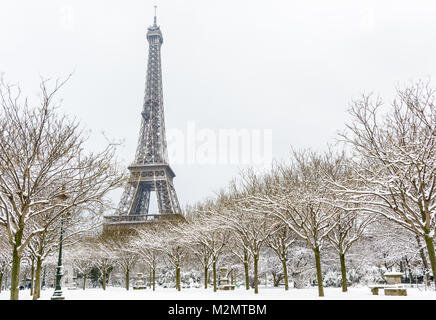 Winter in Paris im Schnee. Der Eiffelturm vom Champ de Mars mit einem schneebedeckten Allee im Vordergrund gesäumt. Stockfoto