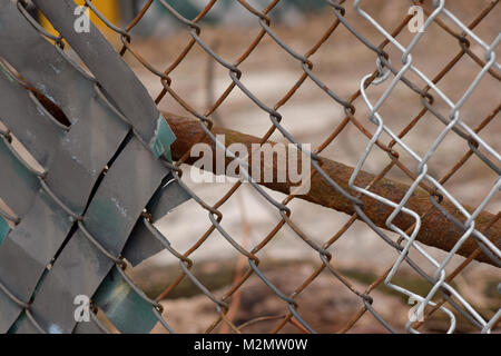 Rusty Maschendrahtzaun mit einer braunen und grauen städtischen Hintergrund verschwommen im Bokeh. Stockfoto