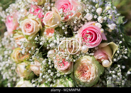 In der Nähe von romantischen frischen bunten Hochzeit Blumenstrauß aus Rosen geschmückt mit kleinen weißen wilden Feldblumen mit zwei bridal Ringe von Braut und Bräutigam in Sunn Stockfoto