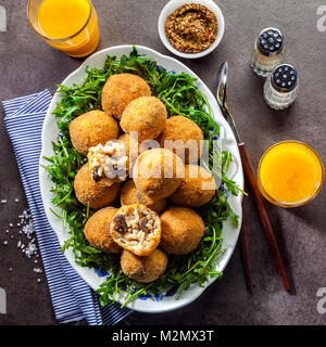 Italienische Snacks. Frittierte Kugeln aus Reis Arancini mit Pilzen, Käse mit Senf Sauce und Salat mit Ruccola auf grauem Stein Tabelle mit frisch Squee Stockfoto