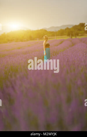 Junge Frau trägt blaue Kleid in einem Lavendelfeld posieren. Konzept positive Stimmung. Weichzeichner Effekt und bokeh Unschärfe-Effekten im Hintergrund. Stockfoto