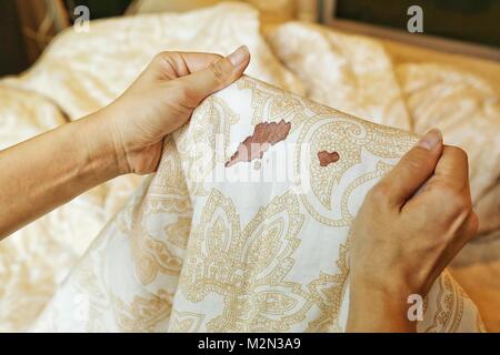 Frauen halten Bettlaken mit Zeitraum Blut Fleck Flecken auf unscharfen Hintergrund. Müssen gereinigt werden. Stockfoto