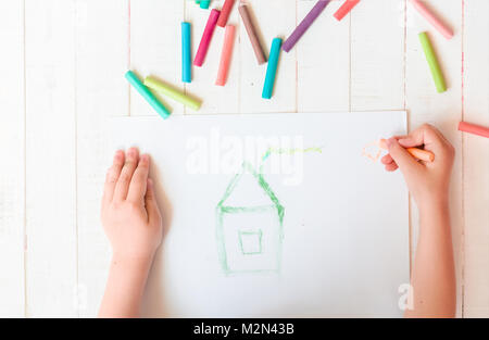 Ein Kind zeichnet ein Haus mit Buntstiften. Haus. Bunte Malstifte, Pastell. Stockfoto