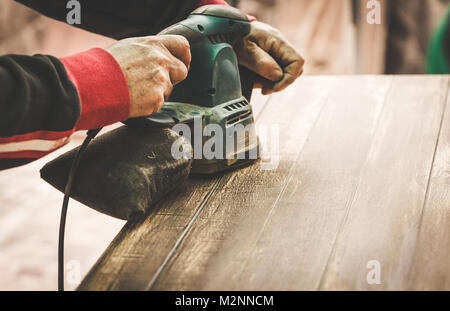 Handwerker Hände polieren alte Farbe von Holztisch mit Maschine. Getönten Bild. Stockfoto