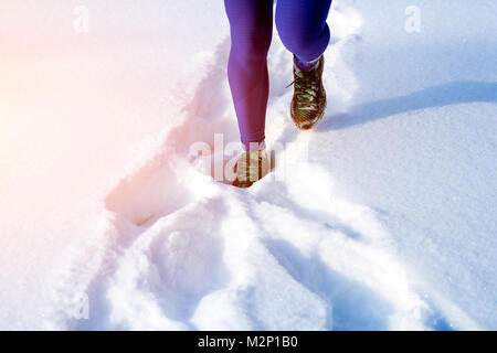 Nahaufnahme einer jungen Frau in hell lila Leggings und Sneakers durch den Winter Schnee auf einem hellen Wintertag, die Vorderansicht Stockfoto