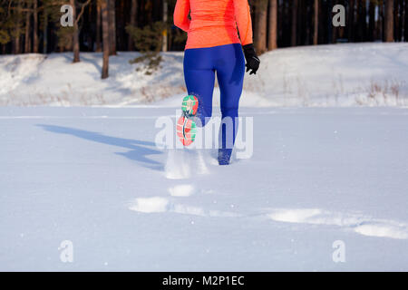 Nahaufnahme einer jungen Frau in hell lila Leggings und Sneakers durch den Winter Schnee auf einem hellen Wintertag, Ansicht von hinten. Im Anschluss an einen s Stockfoto