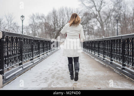 Eine Frau, die zu Fuß über die Brücke im Stadtpark mit Schnee und zurück auf die Kamera Stockfoto