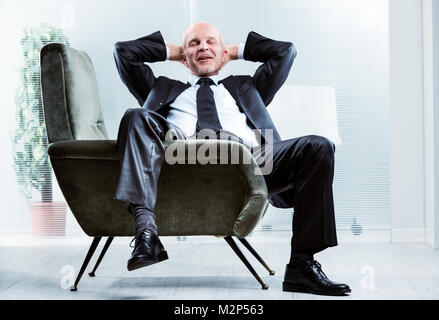 Unternehmer sitzen, entspannen und in einem bequemen Sessel mit seinem Bein über der Seite drapiert, die Hände in den Nacken, schloss die Augen und eine ha Stockfoto