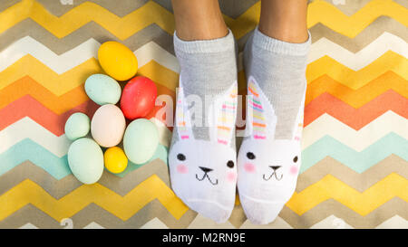 Spaß helle und farbenfrohe Flach der Person tragen bunny Socken mit Ostereier auf moderne Chevron gemusterten Picknickdecke oder Stoff. Platz kopieren Stockfoto