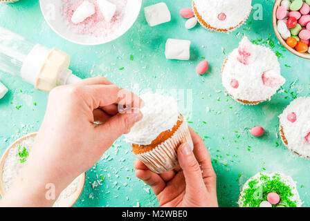 Die Ostern Cupcakes, Person dekorieren Kuchen mit Hasenohren und Candy Eier, copy space frame Ansicht von oben, das Mädchen Hände im Bild Stockfoto