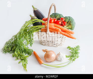 Gesunde Ernährung Konzept: frisches Gemüse in einem weißen Warenkorb: Auberginen, Möhren, Brokkoli und Tomaten zusammen mit einer Zwiebel, Knoblauch und eine kleine Karotte Stockfoto