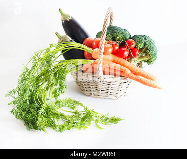 Gesunde Ernährung Konzept: frisches Gemüse in einem weißen Warenkorb: Auberginen, Möhren, Brokkoli und Tomaten zusammen mit einer Zwiebel, Knoblauch und eine kleine Karotte Stockfoto