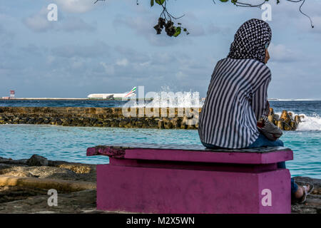 Muslimische Frau am Strand von Männlichen mit Blick auf sterben Flughafeninsel Hulule mit landendem Flugzeug Stockfoto