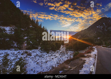 Sonnenuntergang an der schneebedeckten Mount Baldy im Winter mit einer Straße windet sich durch die hohen Gipfel und bunte Wolken im Himmel, San Gabriel Mountains Stockfoto