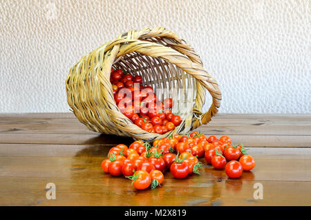 Kirsche Tomaten rollen außerhalb der Korb auf einem Holztisch Stockfoto
