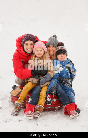 Bild der glücklichen Familie mit Tochter und Sohn sitzen auf Schläuche im Winter Stockfoto