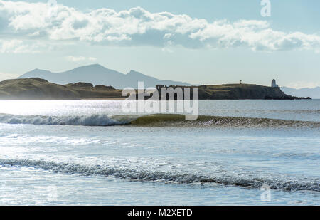 Ein peeling Wave vor der Twr Mawr Leuchtturm auf llanddwyn Insel Anglesey. Die Berge von Snowdonia sind in der Ferne. Stockfoto