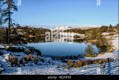 Loughrigg Tarn im Winter mit den Langdale Pikes hinter an einem kalten und schneereichen Februar morgen Stockfoto