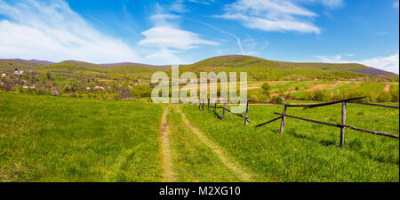 Panorama der bergigen ländlichen Gegend im Frühling. schöne Landschaft Landschaft mit hölzernen Zaun entlang der Landstraße im Dorf Stadtrand Stockfoto