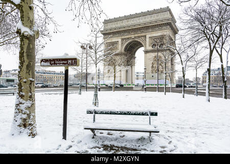 Winter in Paris im Schnee. Der Triumphbogen mit einer öffentlichen Bank im Schnee im Vordergrund verdeckt. Stockfoto