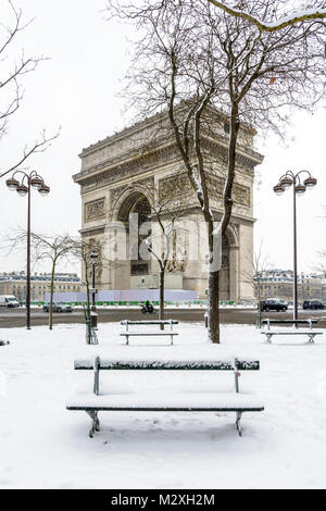 Winter in Paris im Schnee. Der Triumphbogen mit einer öffentlichen Bank im Schnee im Vordergrund verdeckt. Stockfoto