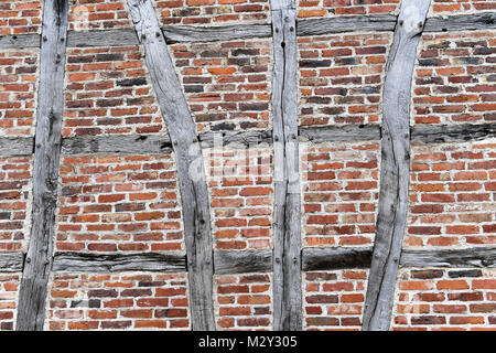 Eine rustikale Ziegelwand mit sichtbaren Holzbalken, die in traditionellem Fachwerkstil angeordnet sind und die natürlichen Texturen, Ziegelsteine und veraltetes Holz zeigen Stockfoto