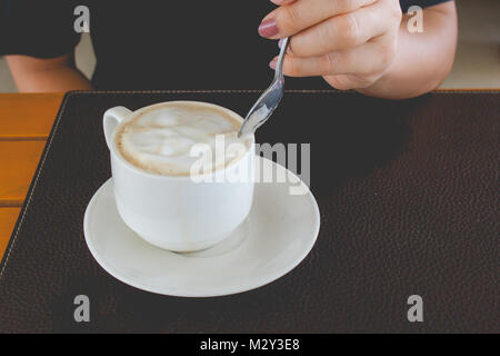 Frau hand Kaffeelöffel und mitreißend heißen Kaffee in Weiß Becher auf hölzernen Tisch im Cafe im Vintage Style. Stockfoto