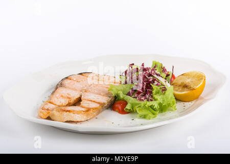 Gebratenes Lachssteak mit Zitrone und Salat auf einem weißen Teller isolieren Stockfoto
