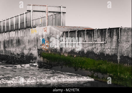 Schwarz-weiß Foto von einem Strand Steg an der kalifornischen Küste mit Graffitis und Moos in Farben bei Dockweiler State Beach in Playa del Rey, CA. Stockfoto