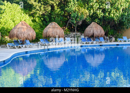 Stroh Sonnenschirme und Sonnenliegen am Außenpool. Riviera Maya, Cancun, Mexiko Stockfoto