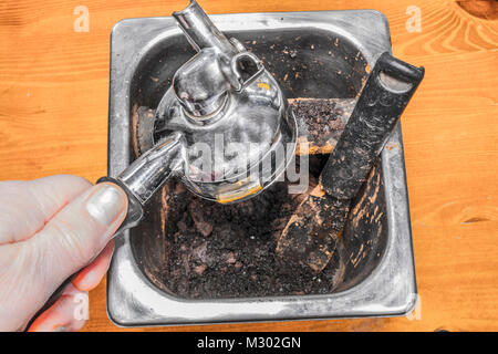 Die Hand des Mannes auf einem portafilter Griff, Entleerung gebrühten Kaffee Anlage/Fugenmörtel in einer Espressomaschine in einen Behälter aus rostfreiem Stahl. England, UK. Stockfoto