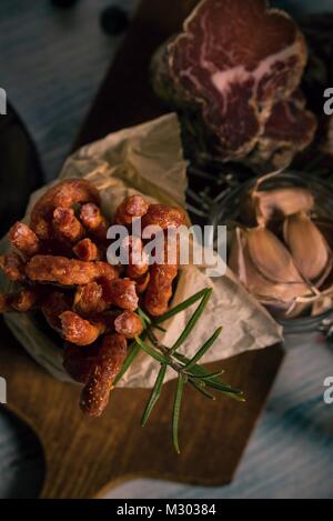 Vertikale Foto mit Top Aussicht auf dünnen Würstchen, die in kann mit Papier im Innern platziert sind. Grüne Rosmarin Zweig neben Salami. Geräuchertes Schweinefleisch ist nächsten Stockfoto