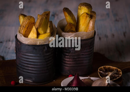 Horizontale Foto von zwei Portionen gebratenen Kartoffeln Streifen mit der Haut. Hausgemachte Pommes Frites sind in alten Vintage Dosen mit Papier im Inneren und auf Platziert abgenutzt Stockfoto