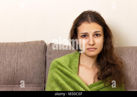 Ein Mädchen verzweifelt Sitzen auf einem beigen Sofa. Frustrierte junge Frau Kopf stirnrunzelnd Suchen unglücklich und stressig. Stockfoto