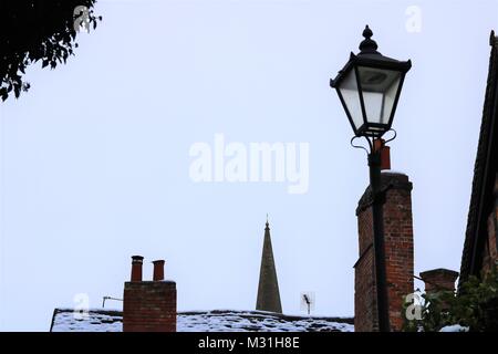 Buckingham, Großbritannien, Skyline Bild der alten Straßenlaterne, chimney pot und Kirchturm mit einem Abstauben des Schnees gegen einen schwachen blauen Himmel im Winter Stockfoto