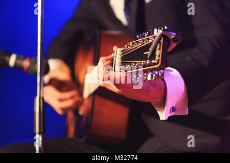Singer's Hände Spielen einer Gitarre Pop oder Klassik Musik auf einem bunten fancy Hintergrund. Mann im eleganten Kostüm spielt die Gitarre während des Konzerts. Stockfoto