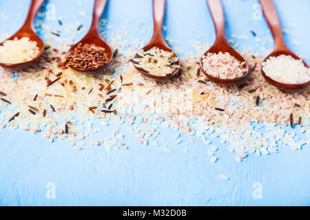 Fünf Löffel mit verschiedenen Sorten Reis auf einem alten Holz- Hintergrund. Zutaten für eine gesunde Ernährung. Stockfoto