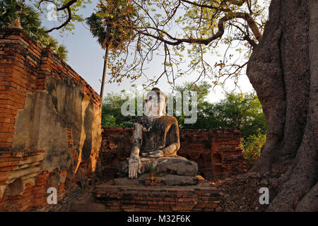 Alte Tempel Ruinen und alte Statue eines sitzenden Buddha gesehen von der Vorderseite der Yadana Hsemee Pagode Komplex in Inwa (Ava) in der Nähe von Mandalay in Myanmar. Stockfoto