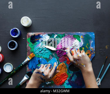 Ansicht von oben, die Hände des Künstlers, der Schöpfer der Farbpalette Bürste, verschiedene Farben. Werkzeuge des Künstlers für reale Kunst und Inspiration. Dark l Stockfoto