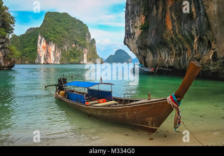 Holz- Boot festgemacht an einem kleinen Strand in einer wunderschönen Bucht zwischen beeindruckenden karstformationen an der Küste von Thailand Stockfoto