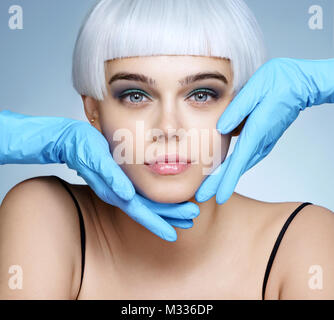 Doctor's Hände in Handschuhen berühren Gesicht der schönen Frau. Foto der Mode blond Modell nach kosmetische Injektion. Ästhetische Kosmetologie Konzept Stockfoto