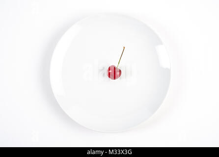 Single Kirsche auf weiße Platte auf weißem Hintergrund. Ansicht von oben. Stockfoto