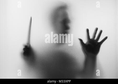 Horror Mörder. Gefährlicher Mann hinter dem Milchglas mit einem Messer auf seine Hand. Halloween Hintergrund. Schwarz-Weiß-Bild Stockfoto