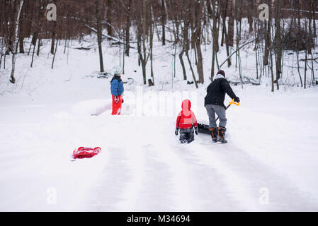 Mann Schneeschaufeln, während seine Kinder eine Schnee fort Bauen Stockfoto